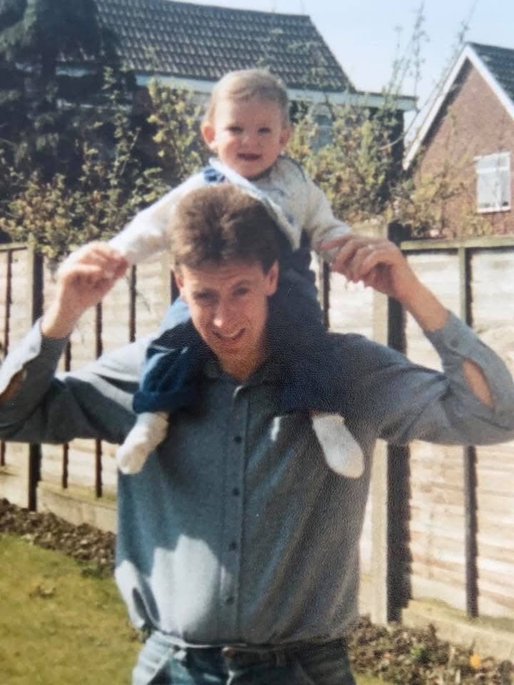 Toddler Chris sitting on his dad's shoulders in the garden